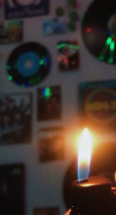 a lit candle sitting on top of a table next to a wall covered in pictures