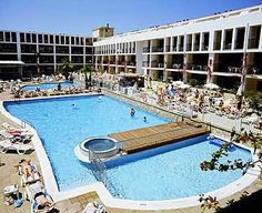 an outdoor swimming pool with people lounging around it and several buildings in the background