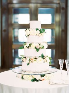 a white wedding cake with flowers and greenery on the top is surrounded by champagne flutes