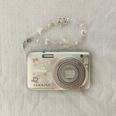 a white camera sitting on top of a bed next to a necklace and bracelet with beads