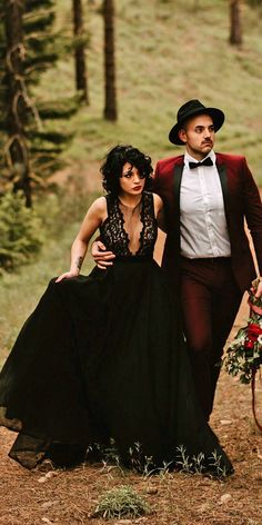 a man and woman dressed in black are walking through the woods with one holding her hand