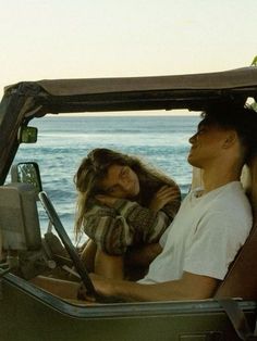 a man and woman are sitting in the back of a jeep with ocean in the background