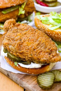 two chicken sandwiches with pickles on a cutting board next to some other food items