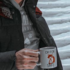 a man holding a coffee mug in his hand while standing next to snow covered ground