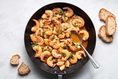 a skillet filled with shrimp and garlic next to slices of bread on a table