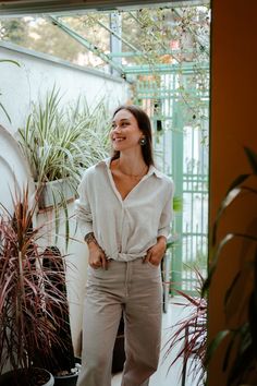 a woman standing in front of some potted plants and smiling at the camera with her hands on her hips