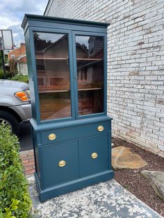 an old china cabinet painted blue with gold handles and knobs on the bottom, in front of a brick building