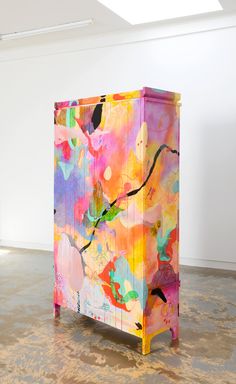 a colorful painted cabinet sitting on top of a floor next to a white wall in an empty room