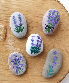 four painted rocks sitting on top of a wooden table next to each other with purple flowers