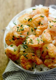 a white bowl filled with shrimp and rice on top of a wooden table next to a fork