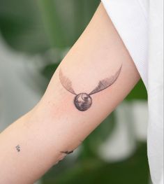 a small tattoo on the arm of a woman with an owl's wing and ball