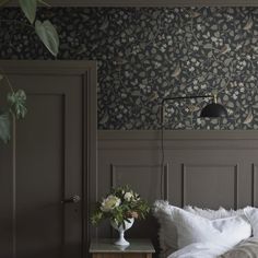 a bedroom with a bed, nightstand and wallpaper in grey tones that has white flowers on it