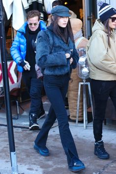 the woman is walking down the sidewalk in her black pants and fur coat, while another man looks on