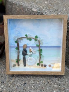 Coastal sea glass bride and groom on a hand painted background. Frame on a 8 1/2 inch by 8 1/2 inch shadow box. Hand painted by CT artist, Raymond White. All sea glass, driftwood, shells, and pebbles collected from beaches all over New England. Great wedding keepsake, bridal shower gift, nautical wedding decor, or wedding gift. Nautical Wedding Decor, Wedding Pictures Beach, Sea Glass Wedding, Picture Beach, Wedding Nautical, Seaside Theme, Background Frame, Glass Wedding, Painted Background