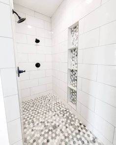 a white tiled shower with black and white tile on the floor, along with shelving unit