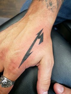 a man's hand with a black lightning symbol tattoo on his left thumb and wrist