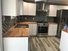 a kitchen with stainless steel appliances and wood counter tops, white cabinets and gray tile backsplash