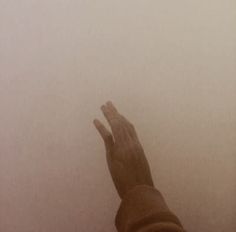 a person reaching up into the foggy sky with their left hand in the air