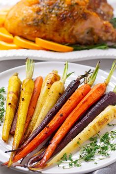 carrots, beets and other vegetables on a white plate next to a roasted chicken