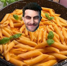 a man's face is surrounded by cooked pasta in a frying pan with basil leaves