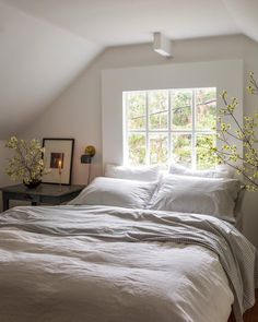 a bed with white sheets and pillows in a room next to a window that has yellow flowers on it