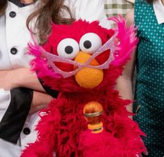 a woman standing next to a red stuffed animal with big eyes and a beak on it's head