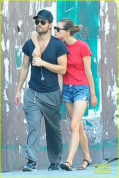 the man and woman are walking together in front of a wall with graffiti on it