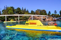 a yellow submarine floating on top of blue water near a bridge in the middle of a river