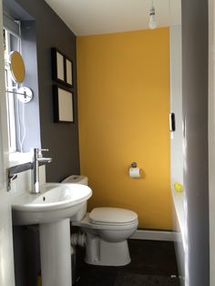 a white toilet sitting next to a sink in a bathroom under a yellow painted wall