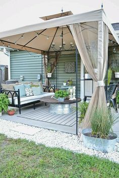 a covered patio with couches and potted plants on the side walk in front of it