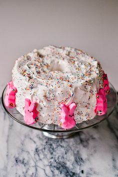 a white cake with sprinkles and pink frosting on a glass plate