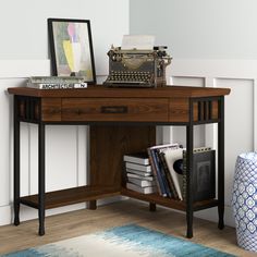 a desk with a typewriter and books on it next to a blue rug in front of a white wall