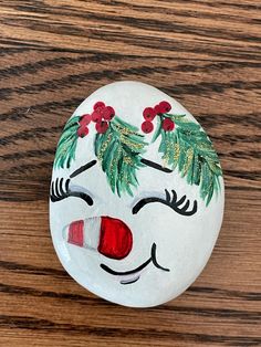 a painted rock with holly leaves and a clown face on it sitting on a wooden surface