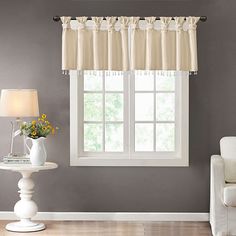 a living room scene with focus on the window curtain and vase full of flowers next to it