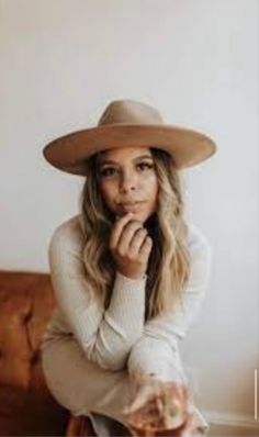 a woman sitting on a couch wearing a hat and holding her hand under her chin