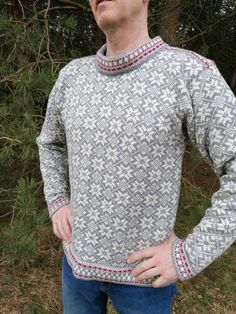 a man standing in front of some trees wearing a sweater with red and white designs on it