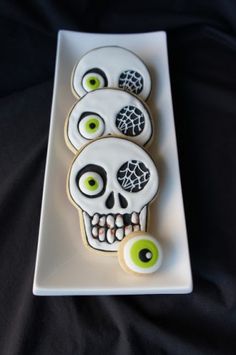 three decorated sugar cookies on a plate with green eyes and black eyeballs in the shape of a skull