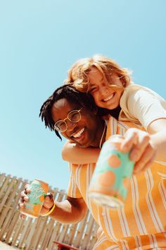 two people are hugging and smiling while holding drinks in their hands, one is wearing an orange striped shirt