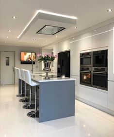 a modern kitchen with white cabinets and counter tops is pictured in this image, the center island has four bar stools on it