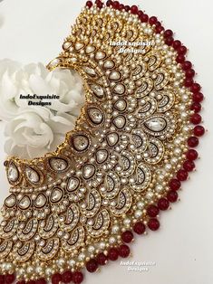 an intricately designed necklace with pearls and red beads on the bottom, along with a white flower