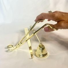 a hand holding a pair of tongs over a metal bell on a white surface