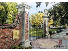 a painting of an iron gate in front of a brick wall and tree lined street