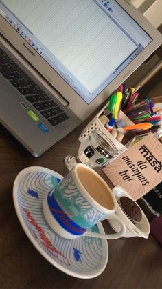 a coffee cup sitting on top of a saucer next to a laptop computer