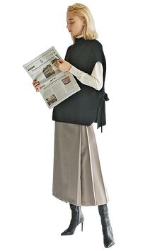 a woman is reading a newspaper while wearing high heeled boots and a black dress