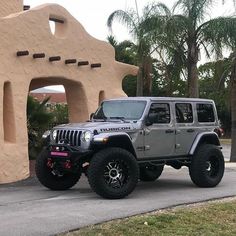 a gray jeep parked in front of a building with an arch on it's side