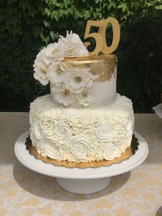 a white and gold wedding cake with flowers on the top is sitting on a table