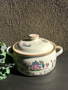 a pot with a lid sitting on top of a table next to some plants and a wall