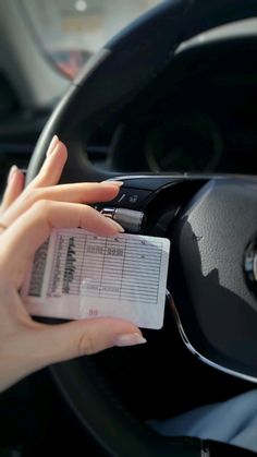 a woman is holding a receipt in her hand while driving a car with the steering wheel behind her