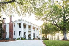 a large white house sitting on top of a lush green field next to tall trees