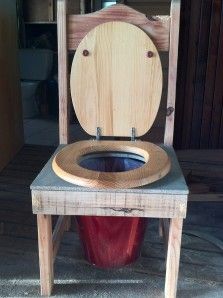 a wooden toilet seat sitting on top of a red trash can next to a chair